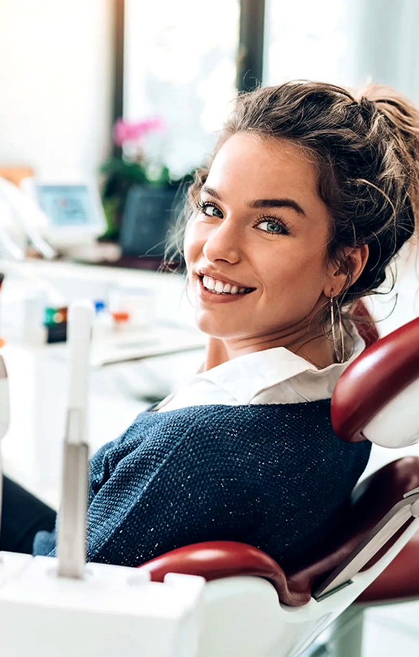 A smiling woman in a dental chair looks back at the viewer, suggesting a positive experience with a dentist providing dental treatment in Fort Worth.